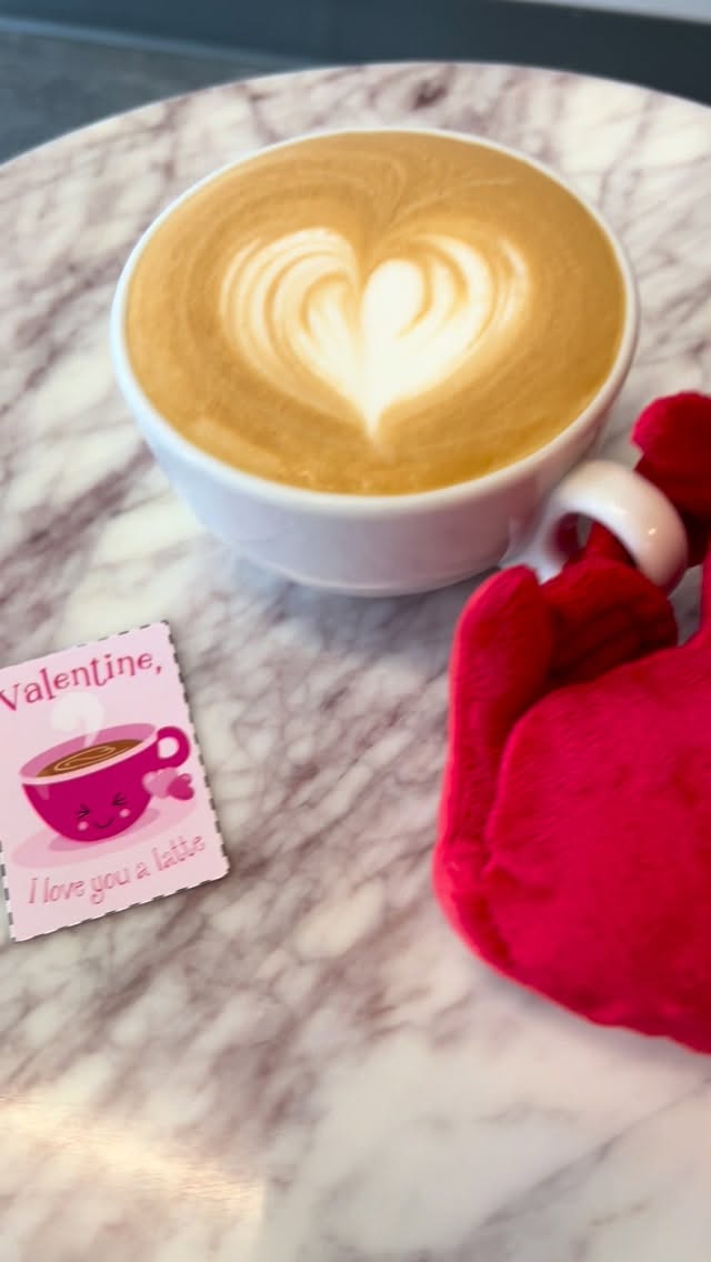 A heart-shaped latte art design on a cappuccino in a white ceramic mug