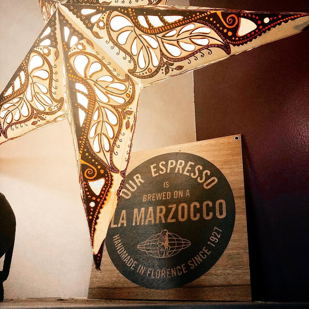 A branded La Marzocco espresso machine sign mounted on a wooden wall